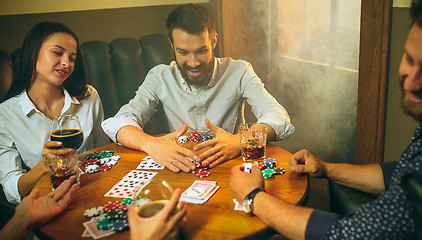 Image showing Side view photo of friends sitting at wooden table. Friends having fun while playing board game.