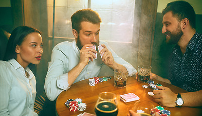 Image showing Side view photo of friends sitting at wooden table. Friends having fun while playing board game.