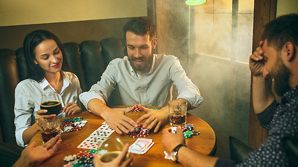 Image showing Side view photo of friends sitting at wooden table. Friends having fun while playing board game.