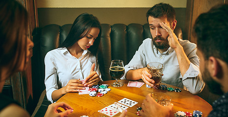 Image showing Side view photo of friends sitting at wooden table. Friends having fun while playing board game.