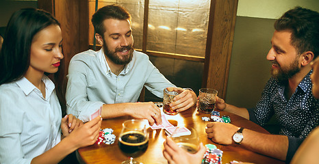 Image showing Side view photo of friends sitting at wooden table. Friends having fun while playing board game.