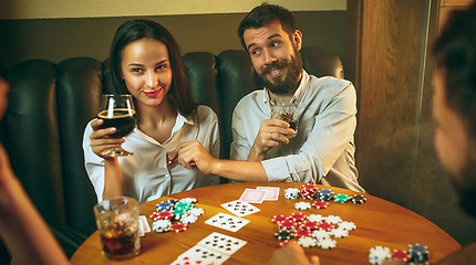 Image showing Side view photo of friends sitting at wooden table. Friends having fun while playing board game.