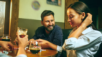 Image showing Side view photo of friends sitting at wooden table. Friends having fun while playing board game.