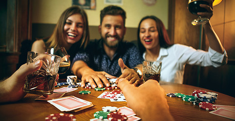 Image showing Side view photo of friends sitting at wooden table. Friends having fun while playing board game.