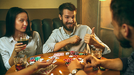 Image showing Side view photo of friends sitting at wooden table. Friends having fun while playing board game.