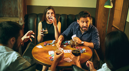 Image showing Side view photo of friends sitting at wooden table. Friends having fun while playing board game.