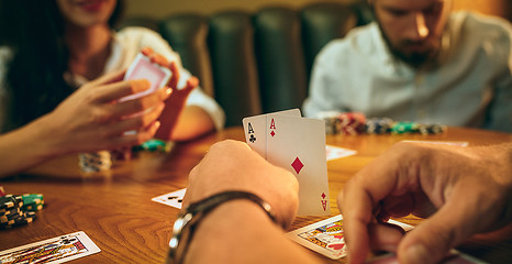 Image showing Side view photo of friends sitting at wooden table. Friends having fun while playing board game.