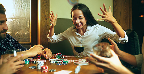 Image showing Side view photo of friends sitting at wooden table. Friends having fun while playing board game.