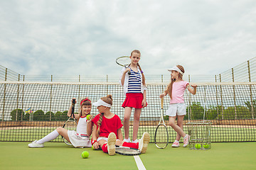 Image showing Portrait of group of girls as tennis players holding tennis racket against green grass of outdoor court