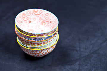 Image showing Stack of colorful empty ceramic bowls closeup on black board bac