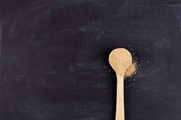 Image showing Brown cane sugar in wooden spoon on black background. 
