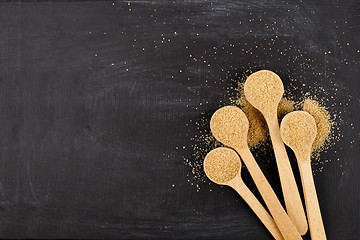 Image showing Brown cane sugar in four wooden spoons on black background.