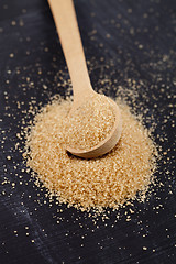 Image showing Brown cane sugar in wooden spoon on black board.