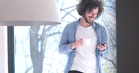 Image showing young man drinking coffee and using a mobile phone  at home