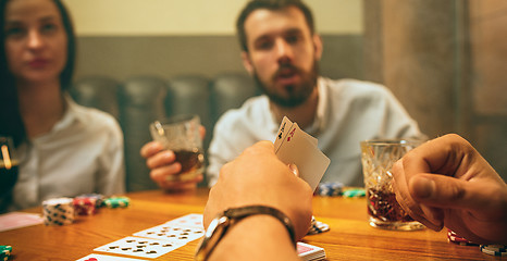 Image showing Side view photo of friends sitting at wooden table. Friends having fun while playing board game.