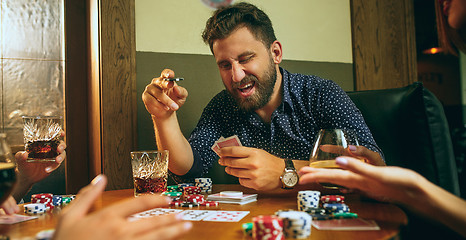 Image showing Side view photo of friends sitting at wooden table. Friends having fun while playing board game.