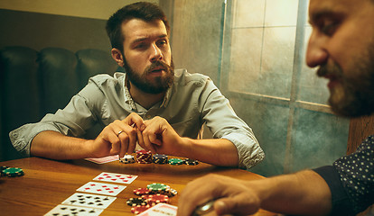 Image showing Side view photo of friends sitting at wooden table. Friends having fun while playing board game.