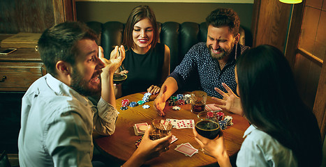 Image showing Side view photo of friends sitting at wooden table. Friends having fun while playing board game.