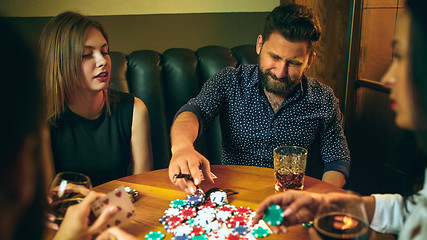 Image showing Side view photo of friends sitting at wooden table. Friends having fun while playing board game.