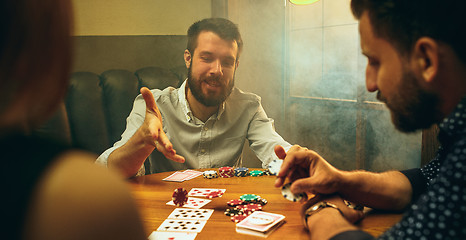 Image showing Side view photo of friends sitting at wooden table. Friends having fun while playing board game.