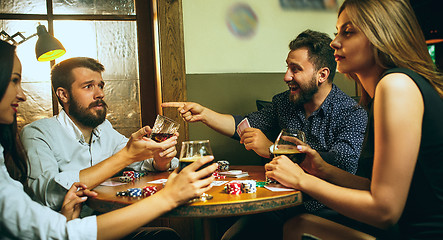 Image showing Side view photo of friends sitting at wooden table. Friends having fun while playing board game.