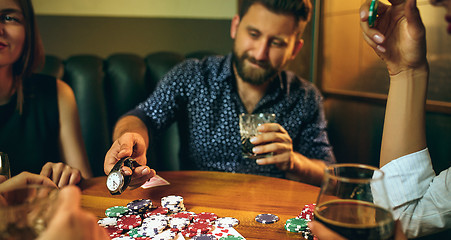 Image showing Side view photo of friends sitting at wooden table. Friends having fun while playing board game.