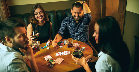 Image showing Side view photo of friends sitting at wooden table. Friends having fun while playing board game.