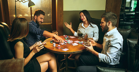 Image showing Side view photo of friends sitting at wooden table. Friends having fun while playing board game.