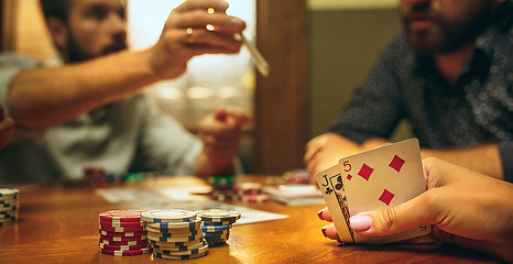 Image showing Side view photo of friends sitting at wooden table. Friends having fun while playing board game.