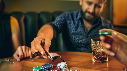 Image showing Side view photo of friends sitting at wooden table. Friends having fun while playing board game.