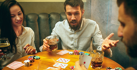 Image showing Side view photo of friends sitting at wooden table. Friends having fun while playing board game.