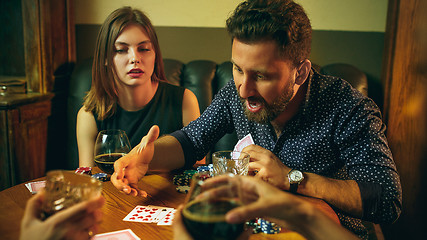 Image showing Friends sitting at wooden table. Friends having fun while playing board game.