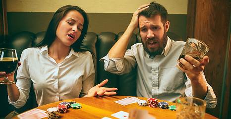 Image showing Side view photo of friends sitting at wooden table. Friends having fun while playing board game.