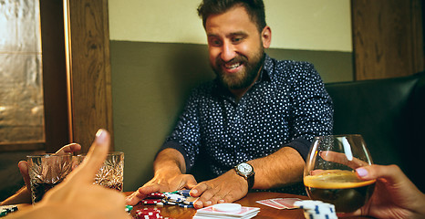 Image showing Side view photo of friends sitting at wooden table. Friends having fun while playing board game.