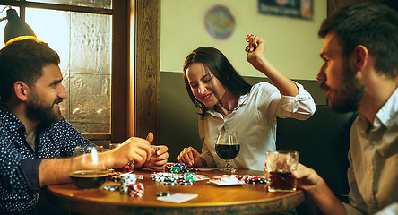 Image showing Side view photo of friends sitting at wooden table. Friends having fun while playing board game.