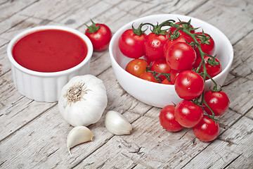 Image showing Fresh tomatoes in white bowl, sauce and raw garlic on rustic woo