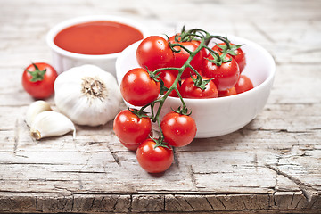 Image showing Fresh tomatoes in white bowl, sauce and raw garlic on rustic woo