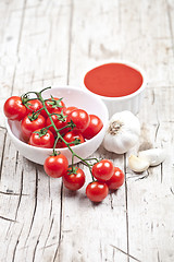 Image showing Fresh tomatoes in white bowl, sauce and raw garlic on rustic woo