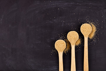 Image showing Brown cane sugar in three wooden spoons on black background. 