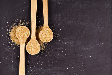 Image showing Brown cane sugar in three wooden spoons on black background.