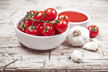 Image showing Fresh tomatoes in white bowl, sauce and raw garlic on rustic woo