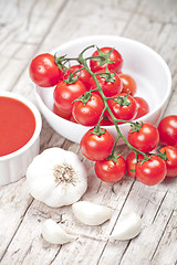 Image showing Fresh tomatoes in white bowl, sauce and raw garlic on rustic woo