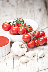 Image showing Fresh tomatoes in white bowl, sauce and raw garlic on rustic woo