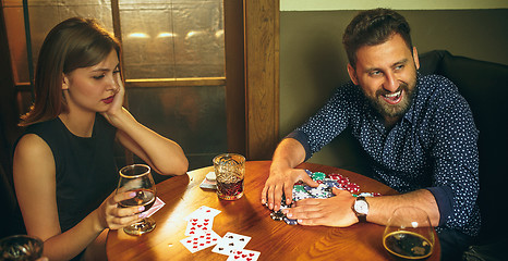 Image showing Friends sitting at wooden table. Friends having fun while playing board game.