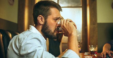 Image showing Side view photo of friends sitting at wooden table. Friends having fun while playing board game.