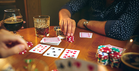 Image showing Side view photo of friends sitting at wooden table. Friends having fun while playing board game.