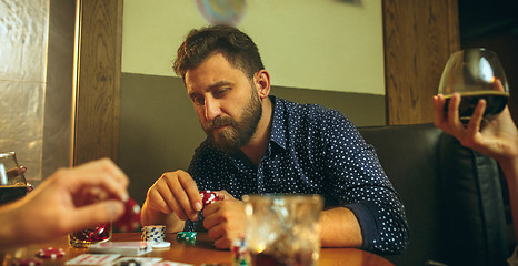 Image showing Side view photo of friends sitting at wooden table. Friends having fun while playing board game.