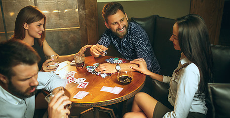 Image showing Side view photo of friends sitting at wooden table. Friends having fun while playing board game.