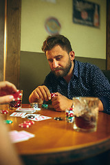 Image showing Side view photo of friends sitting at wooden table. Friends having fun while playing board game.