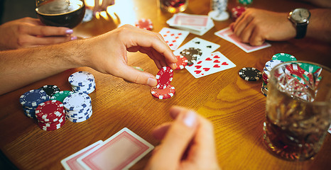 Image showing Side view photo of friends sitting at wooden table. Friends having fun while playing board game.